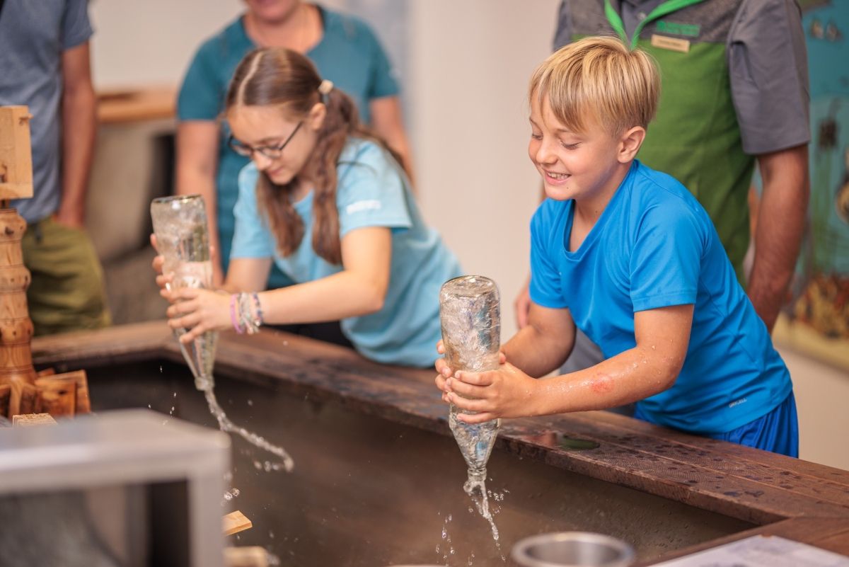 2 Kinder bei einem Versuch mit einer Wasserflasche die sie verkehrt halten